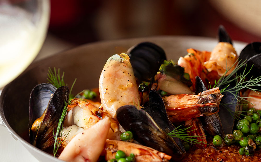 A bowl of rich seafood medley with black mussels, large prawns, and flaky white fish, served at CasCades Restaurant.