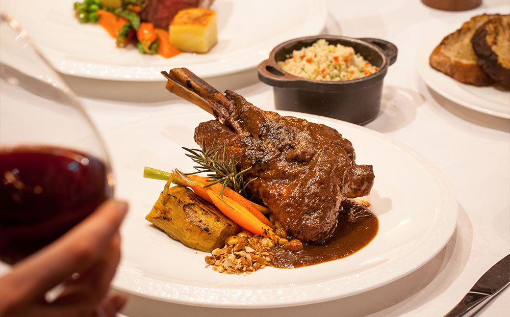 CasCades Restaurant's slow-cooked lamb shank with rich sauce, vegetables, and couscous.