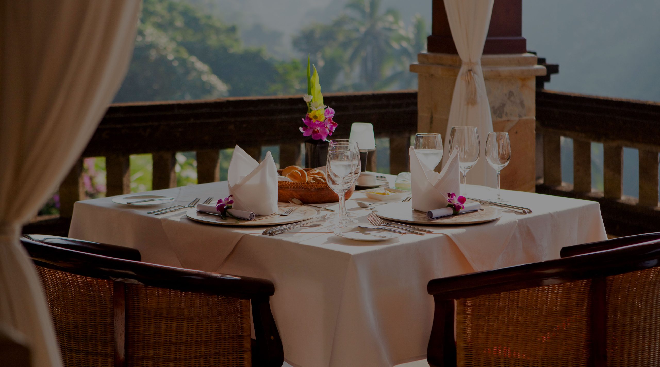 CasCades Restaurant's intimate dining table set for two on a balcony, featuring fresh flowers, crisp white linen, and a romantic jungle valley view in Ubud, Bali.