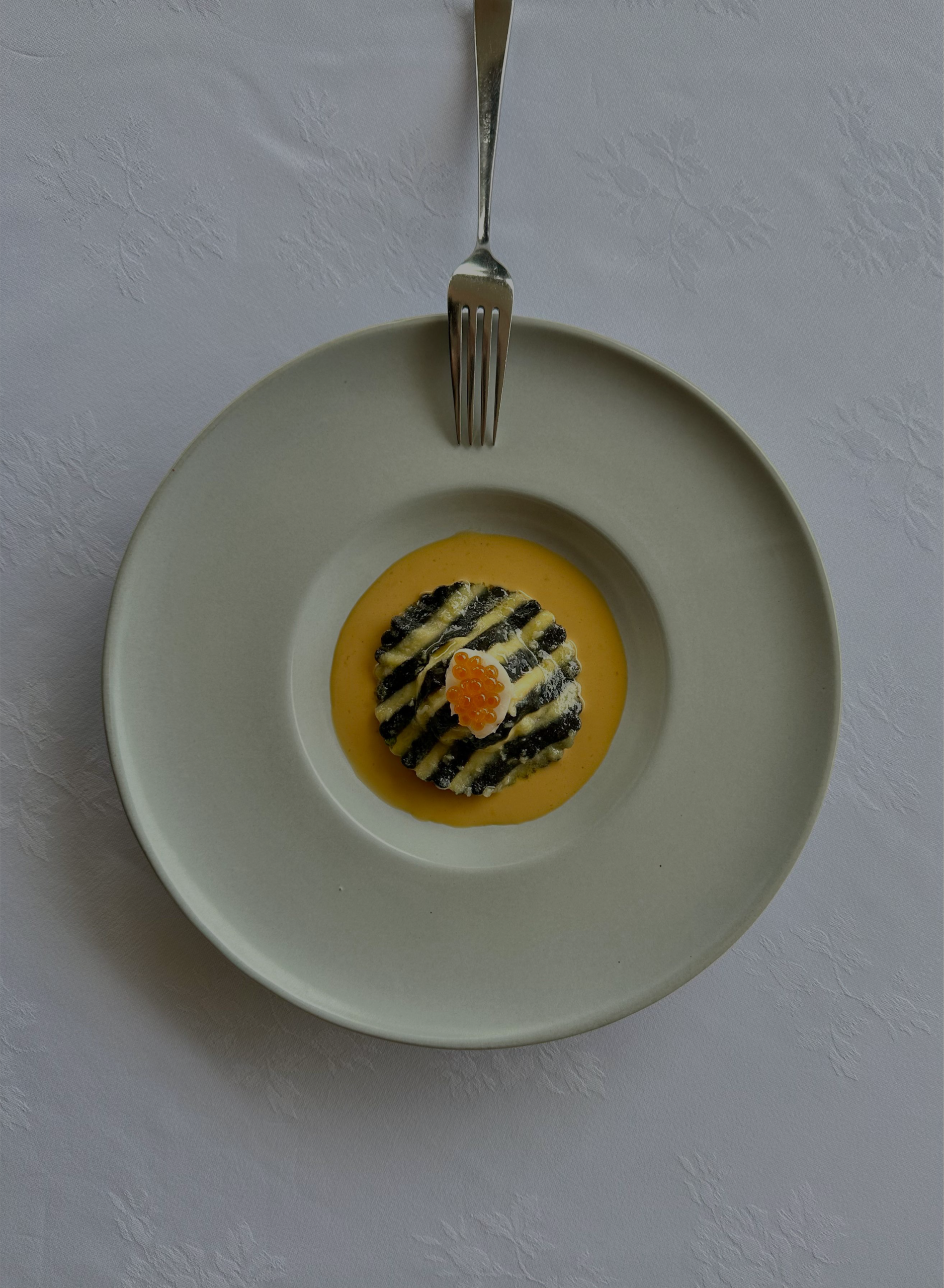 Artistically plated CasCades fine dining dish featuring striped pasta or ravioli in a rich orange sauce, garnished with bright red roe, presented in a minimalist white bowl.
