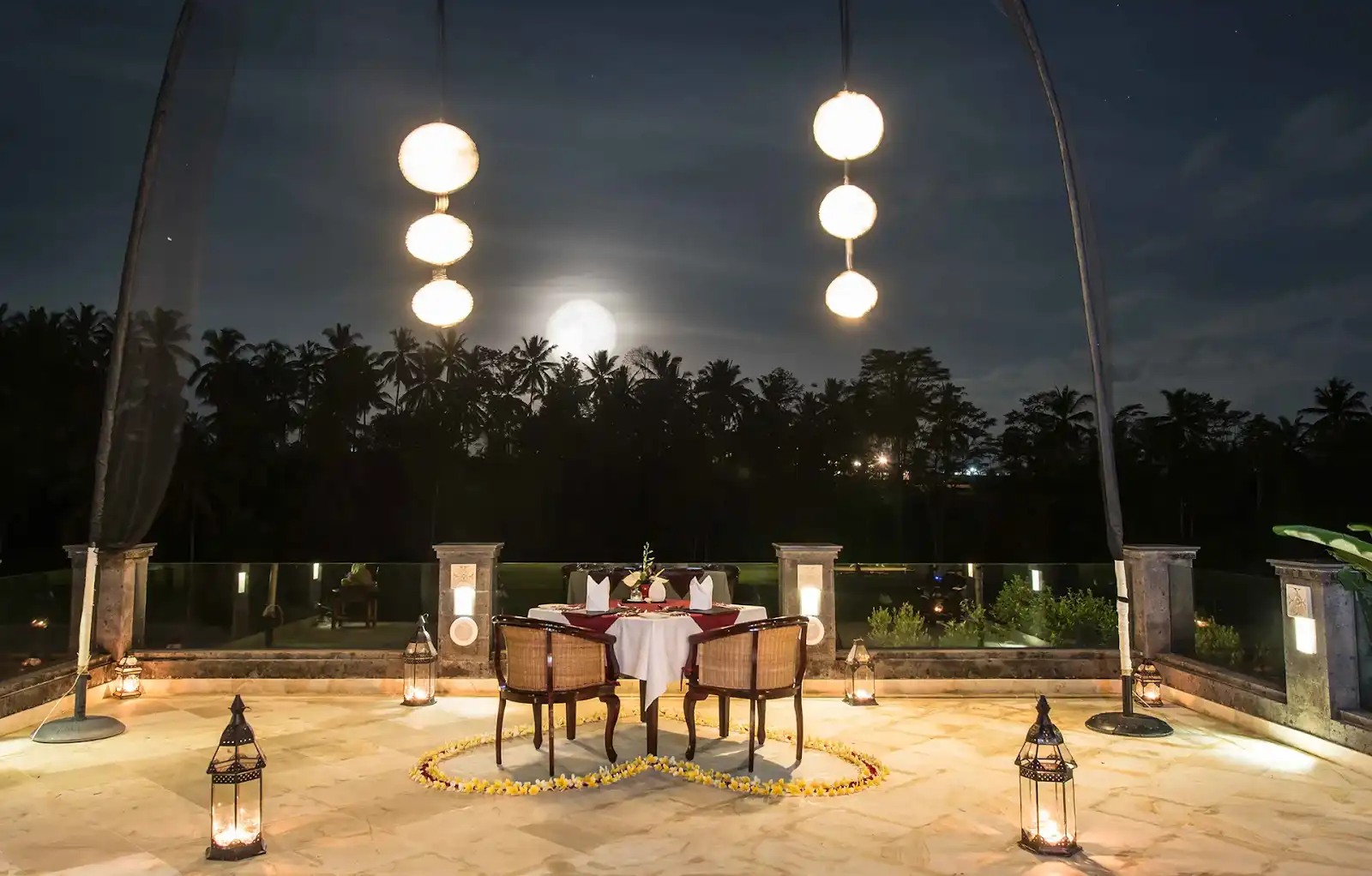 Dining trends in Bali featuring romantic outdoor dinner setup with lanterns, moonlit view, and floral heart décor.